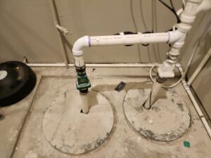 Two sump pits side by side in a basement floor, with a sump pump in only one pit and no backup pump in the overflow pit