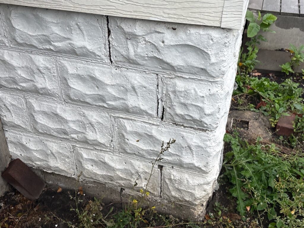 Corner of a painted rock-face concrete block foundation with a stepped crack running through the mortar joints.