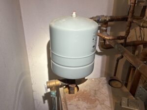 Gray diaphragm expansion tank mounted on the piping of a hot water boiler