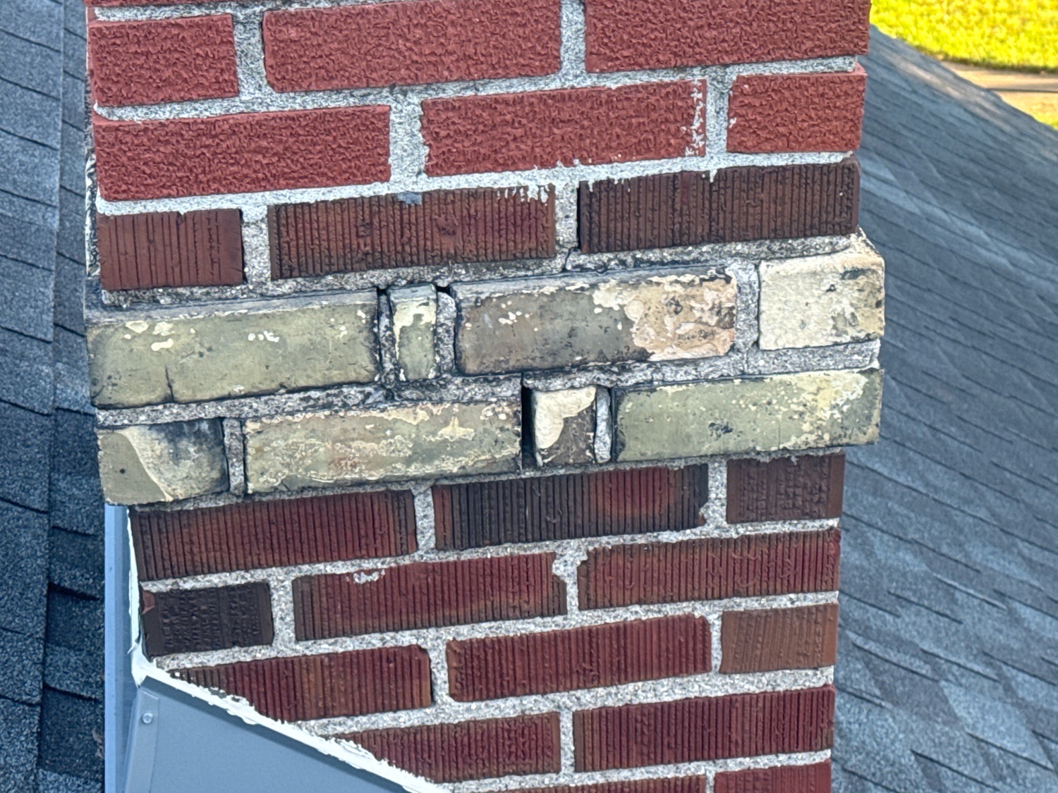 Brick chimney above a roof with washed-out, recessed mortar joints that need tuckpointing