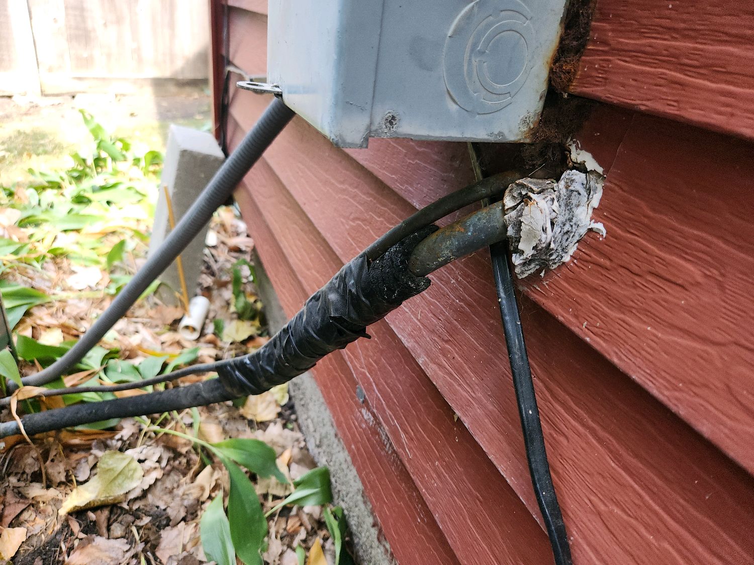 Torn and crumbling foam insulation on an air conditioner refrigerant line where it enters the house