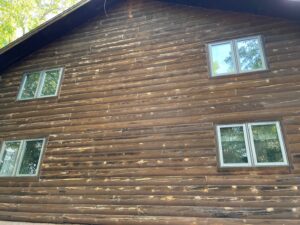 Gable wall of a log home with faded, uneven stain on the logs and three windows
