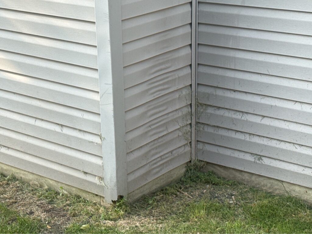 Light gray vinyl siding with a vertical band of rippled panels beside an inside corner.