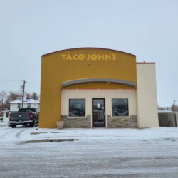 A closed Taco John's restaurant with a snow-covered parking lot and surrounding area on an overcast day.
