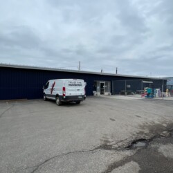 A white van with text "Trust the Norsemen" is parked outside a dark blue industrial building. The sky is overcast.