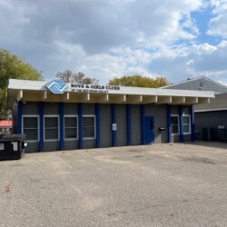 A Boys & Girls Club building with a blue facade and a sign that reads "Boys & Girls Clubs of the Red River Valley" above the entrance. The parking lot in front is empty.
